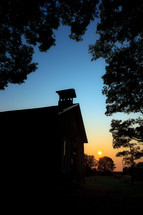 Silhouette of old schoolhouse building in the evening at sunset surrounded by trees 