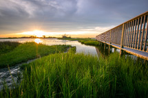 Wooden boardwalk over grassy marsh at sunset with reflection on water
