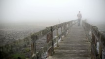 man walking over a boardwalk on a foggy morning 