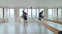 Young ballet couple performing slow synchronic moves with graceful arms and turn in a spacious dance studio with mirror wall. Full shot, copy space
