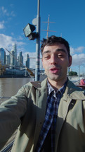 Young handsome male blogger standing outdoors on sunny day, showing the city and telling about it on camera, filming urban or lifestyle vlog. Vertical POV shot
