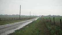 Water covers dirt, country road in rural America during rain storm. Heavy, dramatic, slow motion rain falling on green, summer or spring grass on rural America farmland. Rain waters crops and grass after drought in farming community.