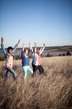 women walking through a field of tall grasses with their hands raised 