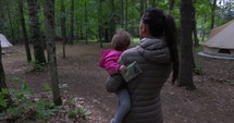Mother carries toddler daughter towards yurt outdoor camping glamping grounds