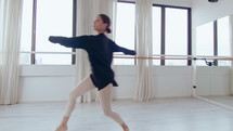 Young inspired ballerina doing arabesque, passe and pirouette while performing graceful dance in studio. Full shot
