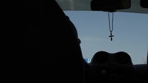 Christian man driving in car with a cross necklace, rosary hanging in windshield on a busy highway with rush hour traffic in city of Dubai in the united Arab emirates.