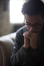 a man in reading glasses with praying hands 