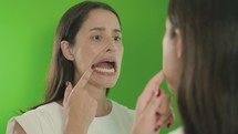 Woman checking her teeth in mirror with opened mouth looking for caries in bathroom at home. Chroma key background. Green screen
