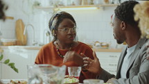 Young cheerful Black couple having discussion and laughing over meal during family dinner at home
