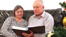 Elderly couple talking near a Christmas tree and looking at a photo album 