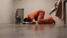 A Christian man in prison laying on ground crying and praying.