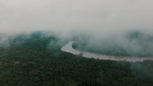 Drone descends through thin clouds over lush Amazon rainforest with a river.