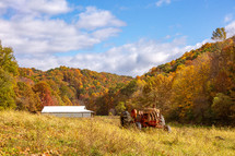 Tractor and barn in grassy field surrounded by trees with autumn fall foliage