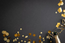Champagne bottle and gold streamers and confetti on a black background with copy space