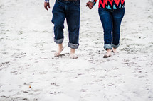 a couple walking through sand holding hands 