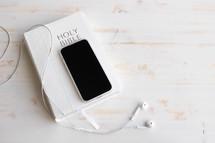 smartphone, earbuds and Bible on a white wood background 