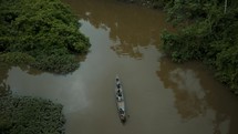 Aerial top down shot of tourists in boat cruising on the Amazon River surrounded by jungle plants in Peru.
