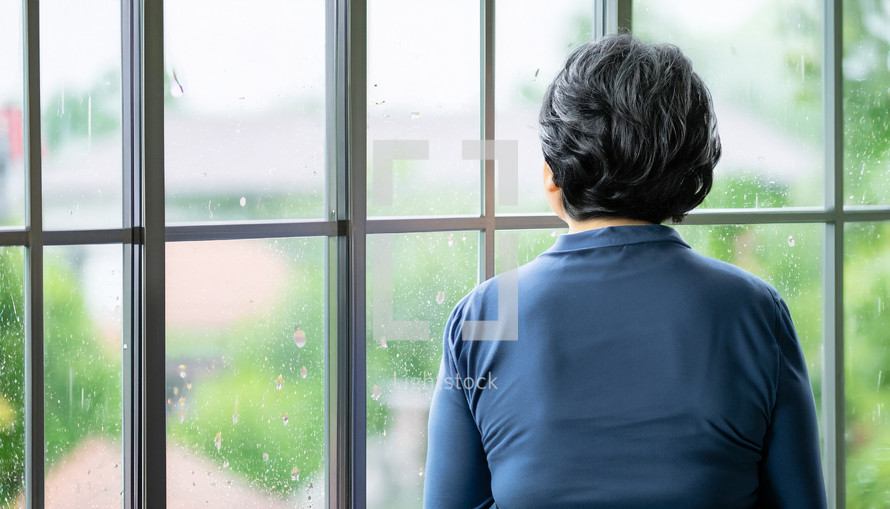 woman with back to the camera looking out a window on a rainy day