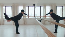 Young professional male dancer performing contemporary style movements and turns, looking at his reflection in the mirror during rehearsal at the studio. Full length shot
