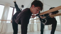 Young male ballet dancer practicing arabesque at the barre, leaning forward and performing tendu in a studio. Zoom Shot
