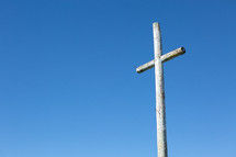 Rustic wooden cross with nails against blue sky 
