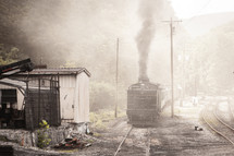 Smoky train engine on tracks passing old shed
