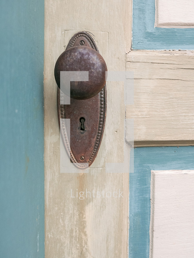 closeup of rusty old door knob and keyhole on painted wooden door