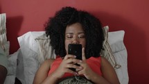 Bored black woman scrolling feed on mobile phone application lying in bed.