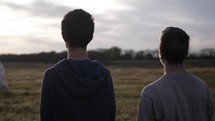 Two young men encounter Jesus, an angel or spiritual figure in white cloak standing in the distance in cinematic slow motion.
