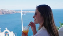 Tourist travel woman in Oia, Santorini, Greece. Happy young woman drinking fresh orange juice enjoying a beautiful view.