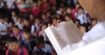 Over the shoulder view of a school teacher reading the Bible to a classroom of students. 