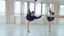 Young professional ballerina doing penche at the barre, leaning forward with one leg raised behind while exercising in dance studio. Zoom shot
