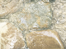 closeup of moving water flowing over large tan rocks