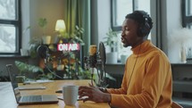 Blogger Reading Script on Laptop and Recording Podcast in Studio
