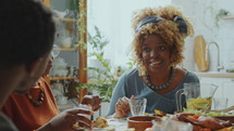 Young African American woman having conversation with family members when having meal at the table during holiday dinner at home
