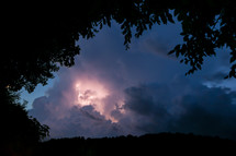 Dramatic lightning storm with dark clouds surrounded by tree silhouette 