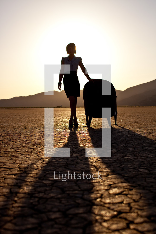 silhouette of a woman standing beside a chair on parched earth