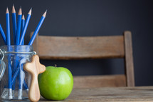 cross, pencils in a jar and apple on a desk 