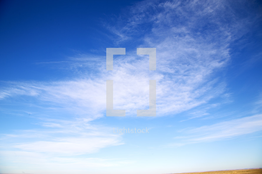white clouds in a blue sky above a desert 