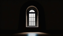 centered, arched window with glow from outside, dark interior with some light streaming in, with copy space