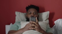 Bored man scrolling feed on mobile phone application lying in bed.