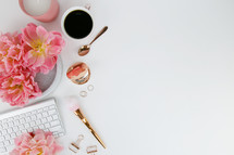 pink spring flowers, computer keyboard, makeup brush, gold hand mirror, rings, coffee mug, and gold spoon on a white background 