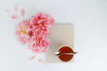 pink spring flowers, tea cup, spoon, and notepad on a desk 