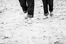 a couple with rolled up jeans walking through the sand 