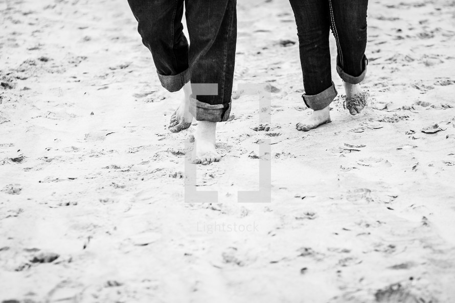 a couple with rolled up jeans walking through the sand 