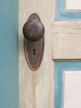 closeup of rusty old door knob and keyhole on painted wooden door