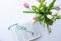 rosary on the pages of a Bible and tulips 