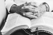 An elderly woman's hands folded on an open Bible.