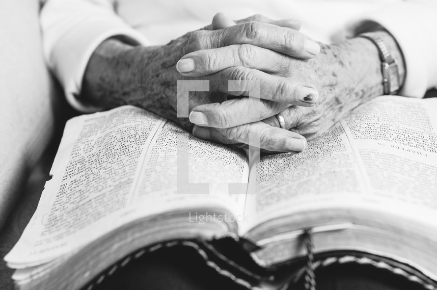 An elderly woman's hands folded on an open bible. — Photo — Lightstock