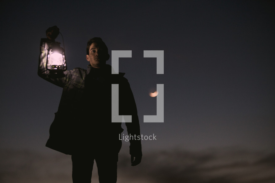 a man holding a lantern outdoors at night 